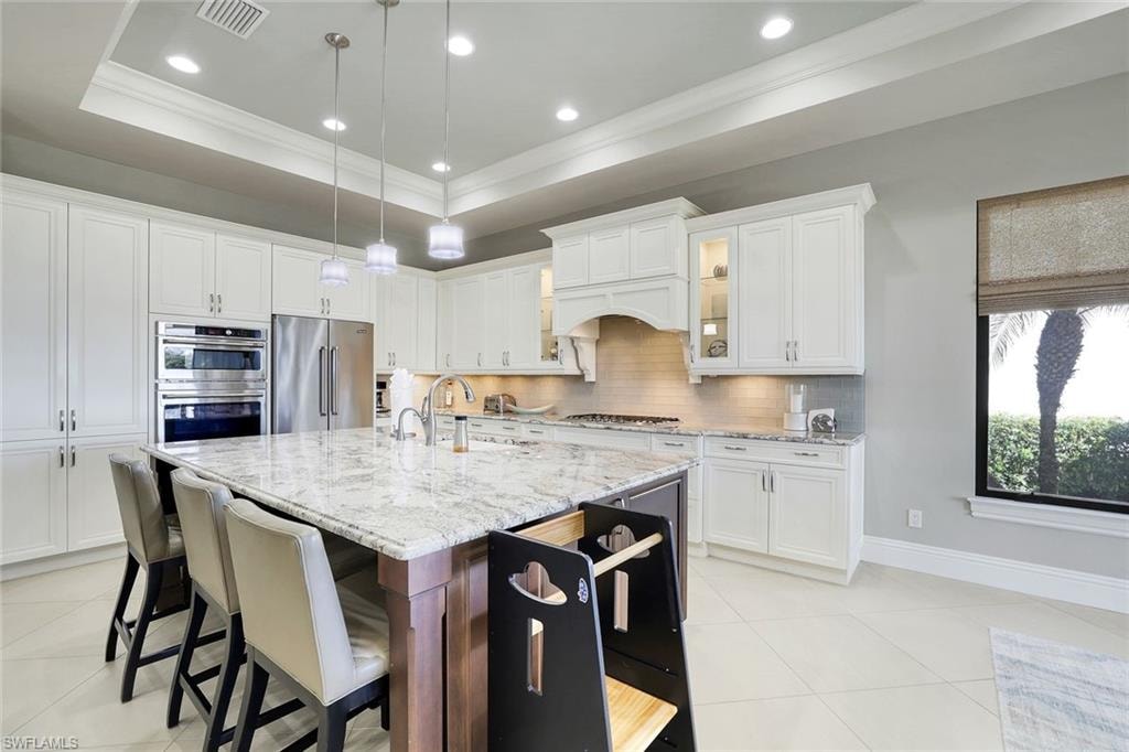 Kitchen with glass fronted cabinets, light stone counters, pendant lighting, white cabinetry, and crown molding