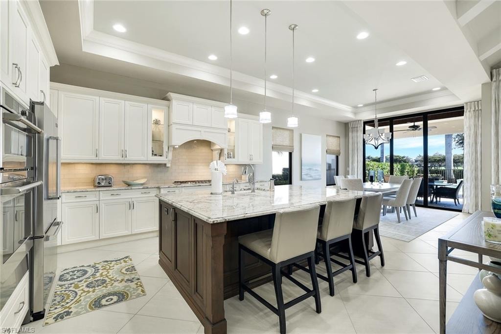Kitchen featuring a tray ceiling, light stone countertops, a kitchen bar, dual tone cabinets, and a large island with sink