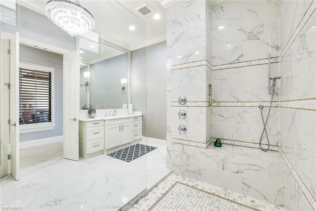 Full bathroom with crown molding, a marble finish shower, vanity, suspended lighting, and light marble finish flooring