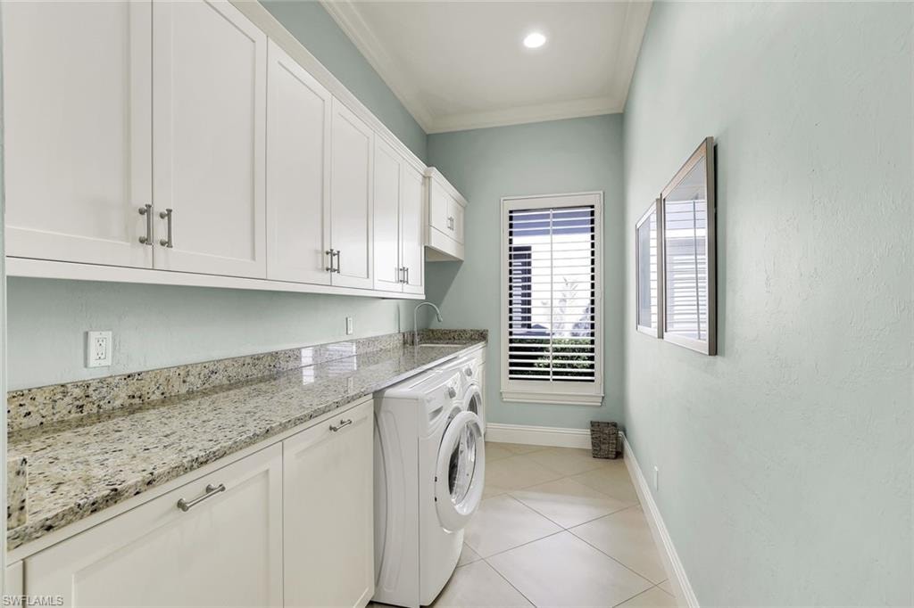 Laundry room featuring cabinet space, crown molding, and light tile patterned flooring