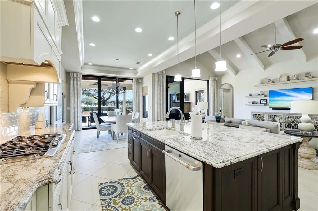 Two tone kitchen featuring two tone cabinets, open floor plan, light stone countertops, stainless steel appliances, and vaulted ceiling with beams