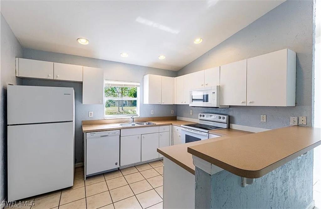 Kitchen featuring white appliances, white cabinetry, a peninsula, lofted ceiling, and a breakfast bar