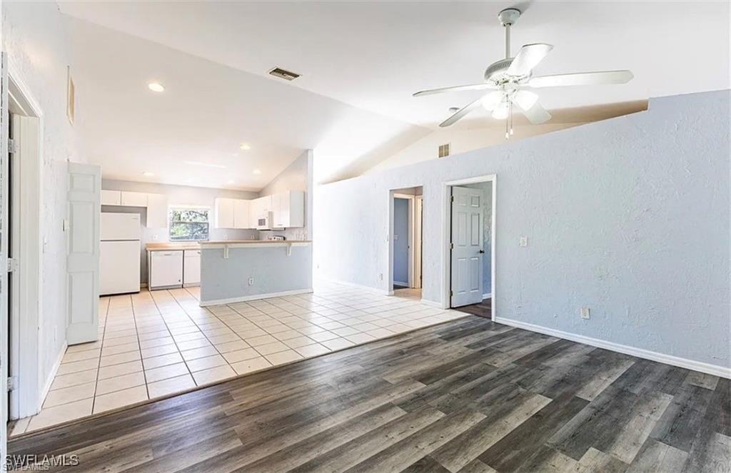 Unfurnished living room with light wood-style floors, vaulted ceiling, a ceiling fan, and a textured wall