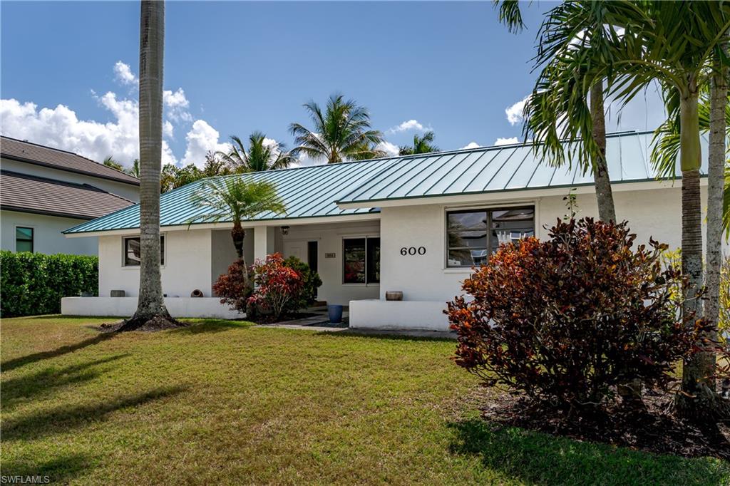 Ranch-style house with a standing seam roof, stucco siding, and a front lawn