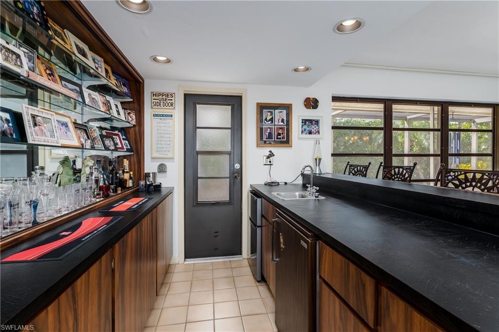 Bar featuring dark countertops, recessed lighting, stainless steel refrigerator, light tile patterned floors, and dark wood finish cabinetry
