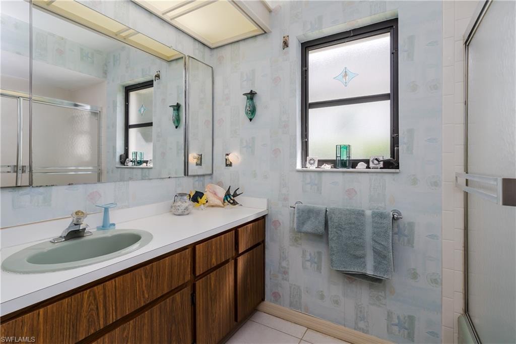 Full bathroom featuring wallpapered walls, vanity, and light tile patterned floors