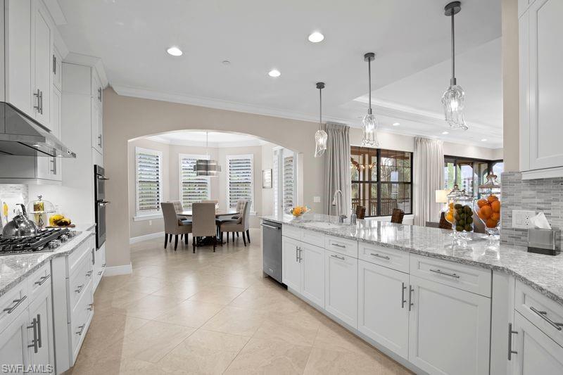 Kitchen with tasteful backsplash, white cabinetry, arched walkways, light stone counters, and ornamental molding