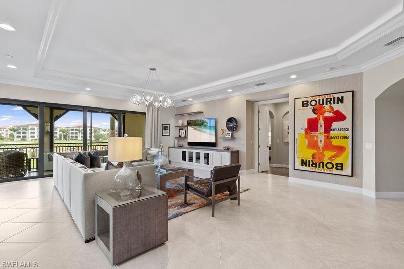 Living room with arched walkways, ornamental molding, a tray ceiling, and hanging lights