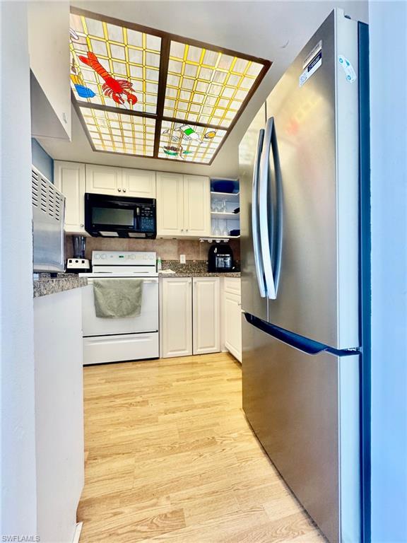Kitchen featuring freestanding refrigerator, white range with electric cooktop, white cabinets, black microwave, and light wood-type flooring