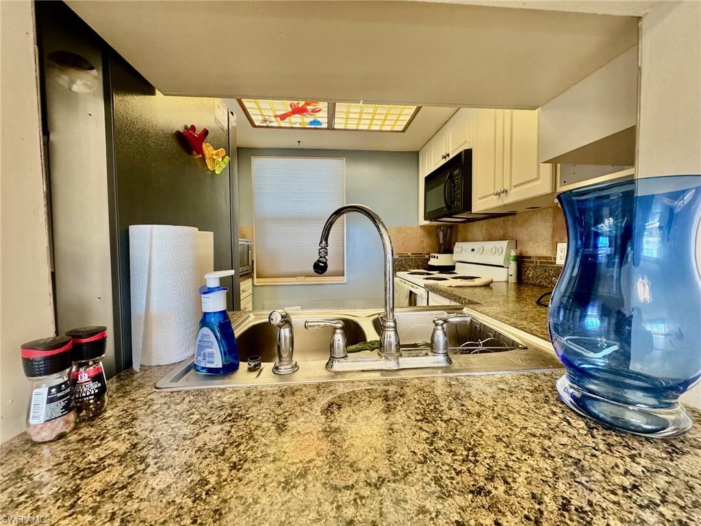 Kitchen with white cabinets, electric stove, black microwave, tasteful backsplash, and light stone counters