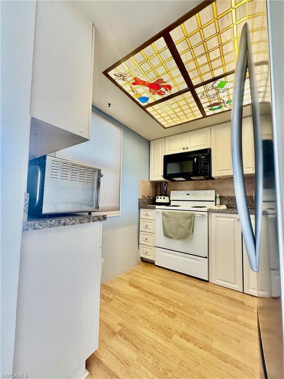 Kitchen with white range with electric cooktop, freestanding refrigerator, white cabinetry, and black microwave
