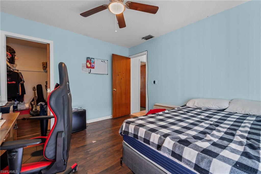 Bedroom featuring dark wood-style floors, a spacious closet, a ceiling fan, a desk, and a textured ceiling