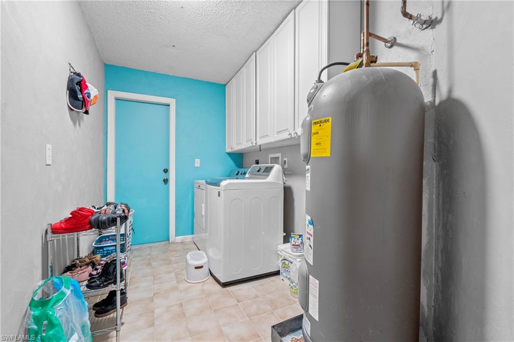 Laundry room with electric water heater, cabinet space, washing machine and clothes dryer, and a textured ceiling