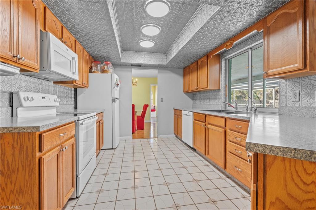 Kitchen featuring white appliances, decorative backsplash, an ornate ceiling, and wood finish cabinetry