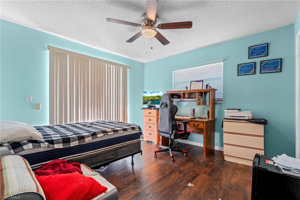 Bedroom featuring dark wood-type flooring, a textured ceiling, a ceiling fan, and a desk