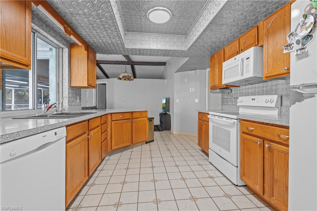 Kitchen with white appliances, a peninsula, light countertops, an ornate ceiling, and tasteful backsplash