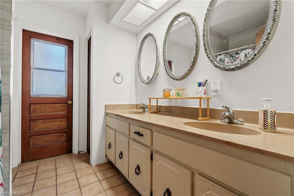 Bathroom featuring tiled shower, double vanity, and light tile patterned floors