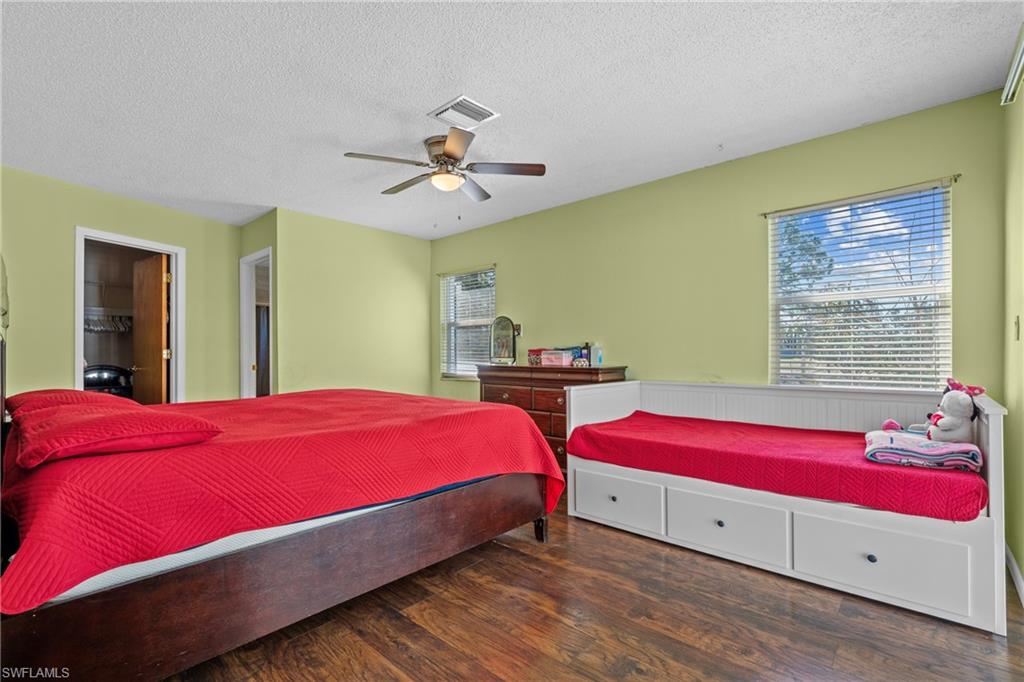 Bedroom featuring dark wood-style flooring, a walk in closet, a textured ceiling, and a ceiling fan