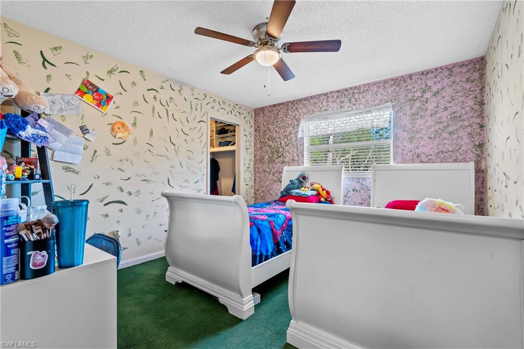 Bedroom featuring wallpapered walls, a textured ceiling, dark colored carpet, and a ceiling fan