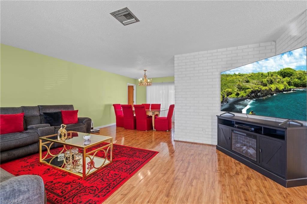 Living room with wood finished floors, suspended lighting, brick wall, and a textured ceiling