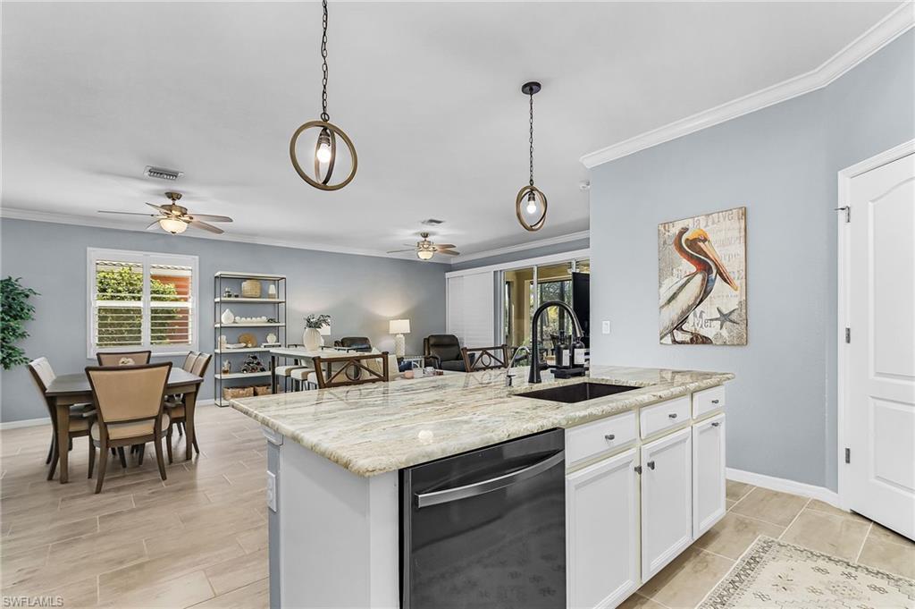 Kitchen with ornamental molding, stainless steel dishwasher, light stone countertops, white cabinets, and an island with sink