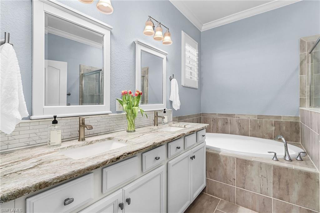 Bathroom with crown molding, double vanity, a bath, and a tile shower
