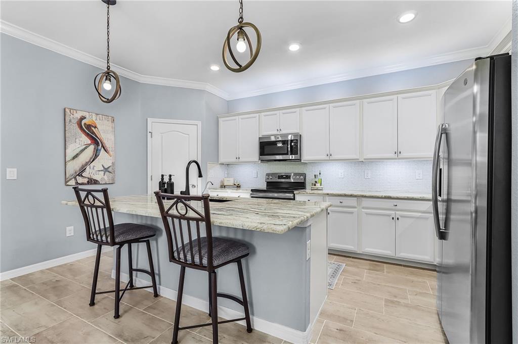 Kitchen featuring stainless steel appliances, white cabinetry, crown molding, tasteful backsplash, and an island with sink