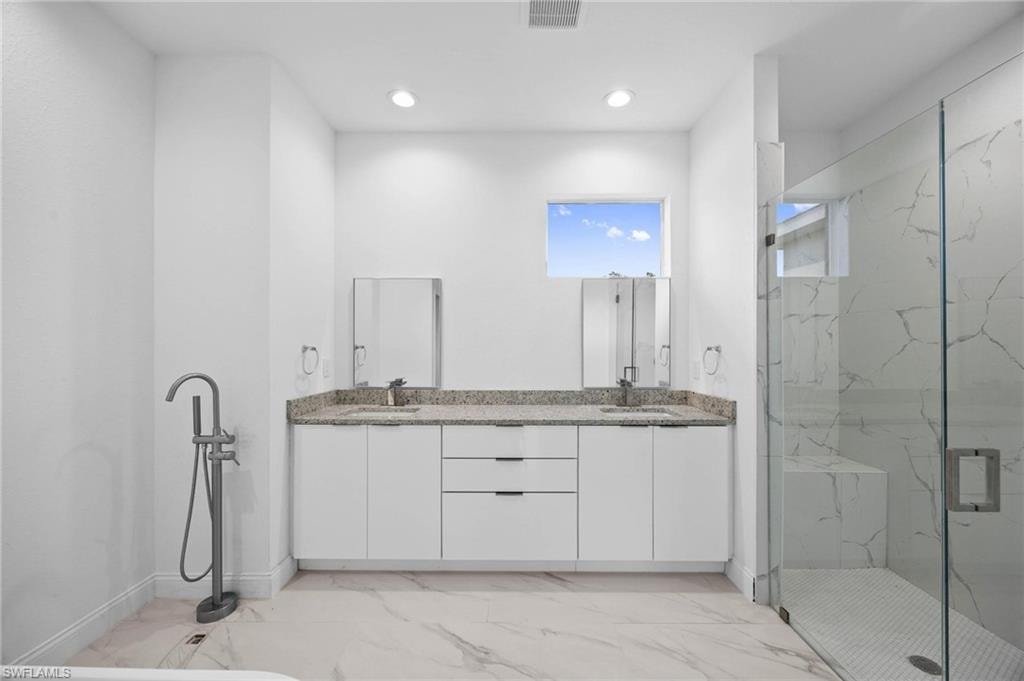 Full bath featuring double vanity, a marble finish shower, light marble finish flooring, and recessed lighting