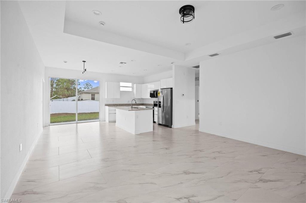 Unfurnished living room with light marble finish flooring, recessed lighting, and a raised ceiling