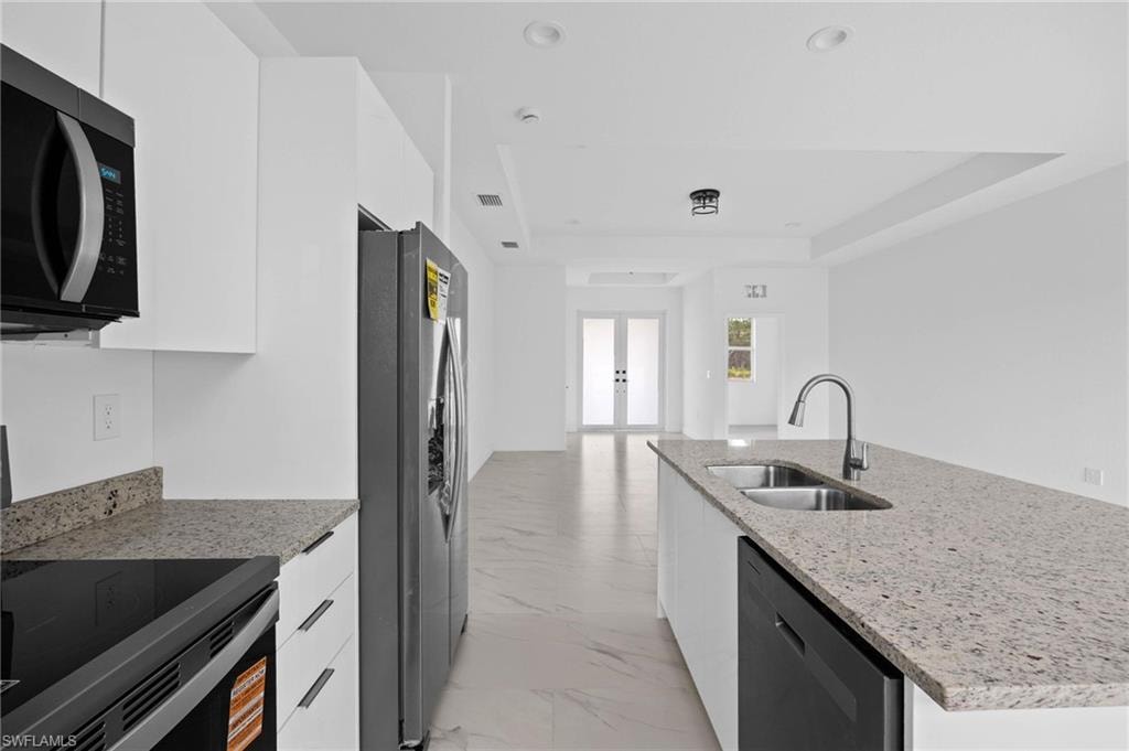 Kitchen with stainless steel appliances, light stone counters, white cabinetry, modern cabinets, and a tray ceiling
