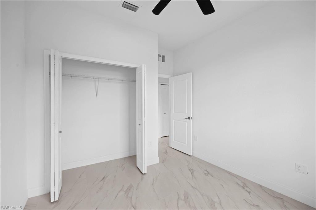 Unfurnished bedroom with light marble finish flooring, a closet, and a ceiling fan