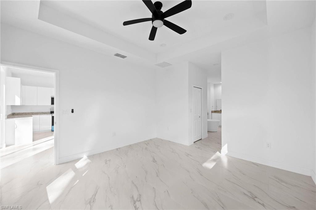 Spare room with a tray ceiling, light marble finish flooring, and ceiling fan