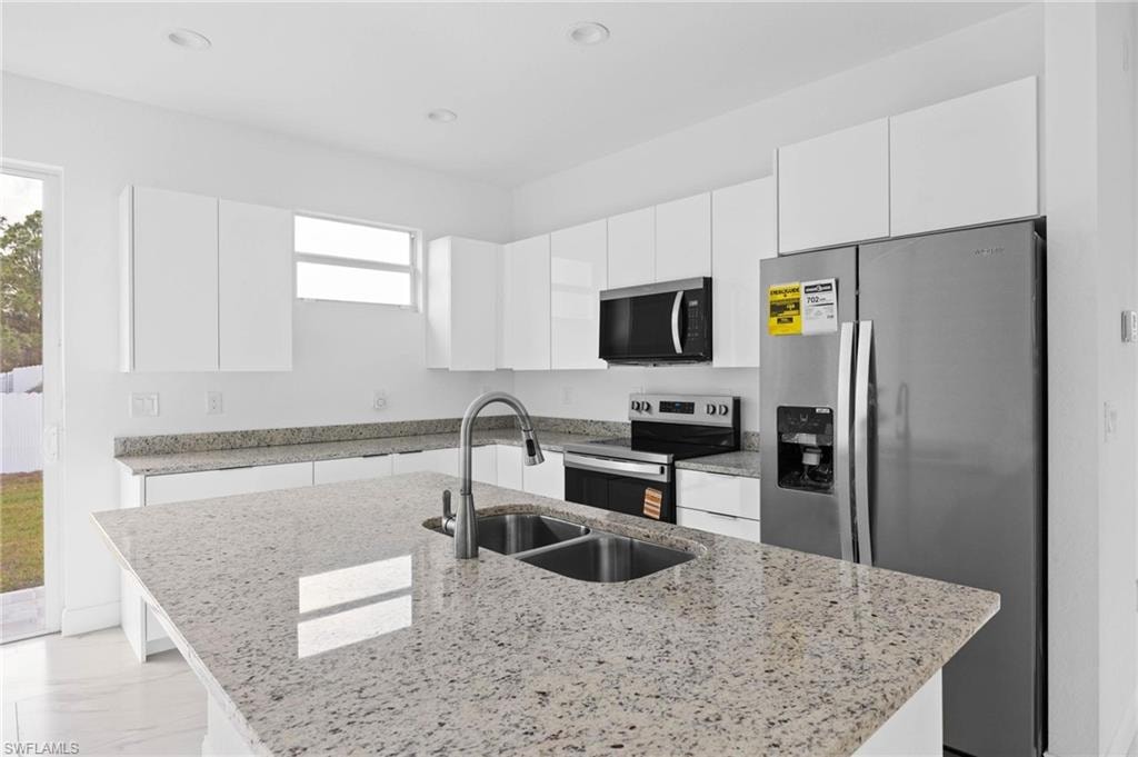 Kitchen featuring stainless steel appliances, white cabinetry, light stone counters, a kitchen island with sink, and recessed lighting