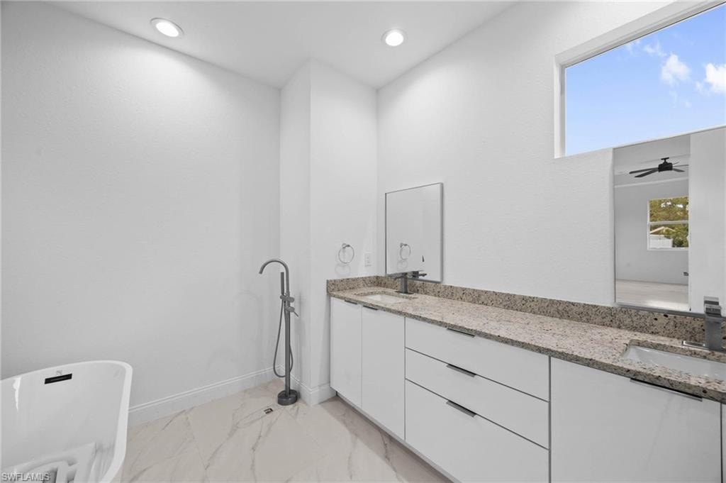 Bathroom featuring a freestanding tub, double vanity, recessed lighting, a ceiling fan, and light marble finish flooring