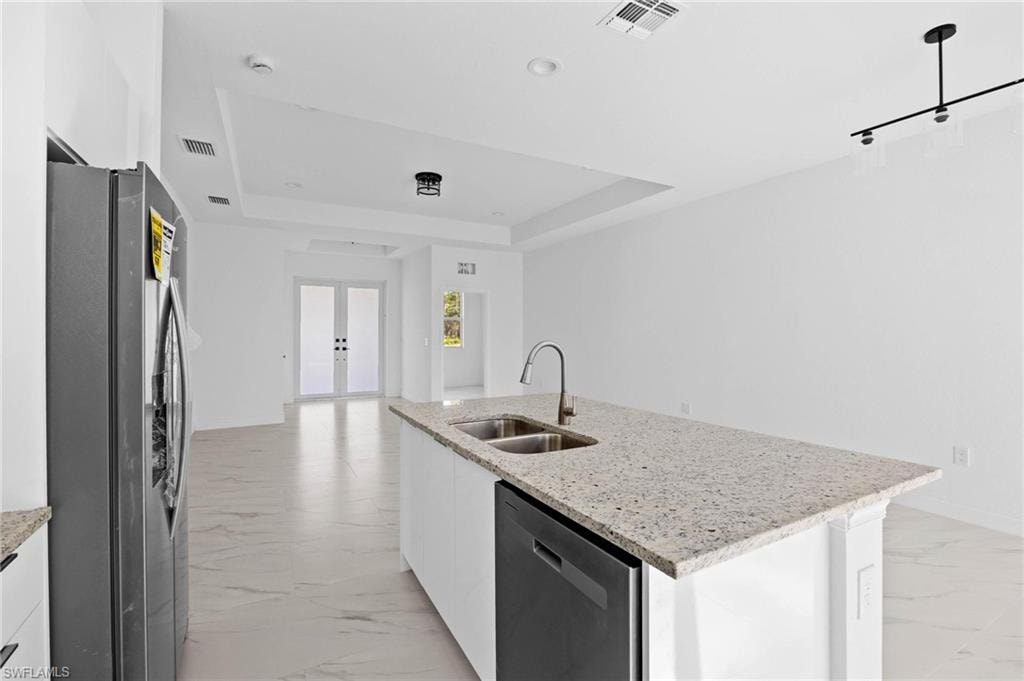 Kitchen with light stone countertops, white cabinetry, stainless steel appliances, modern cabinets, and a tray ceiling