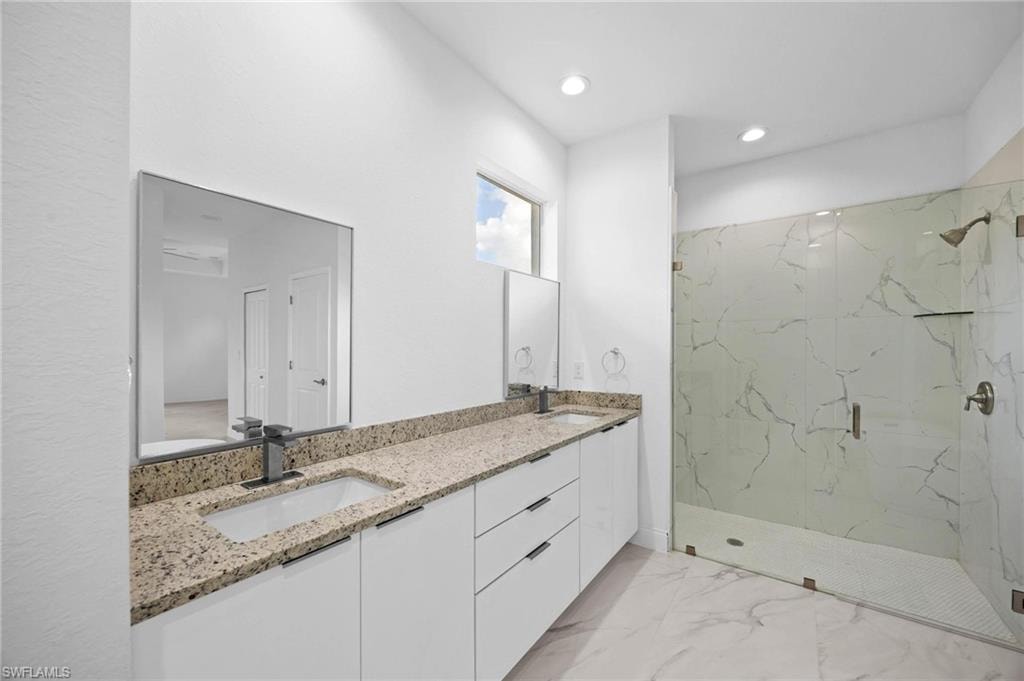 Bathroom with a marble finish shower, double vanity, light marble finish floors, and recessed lighting
