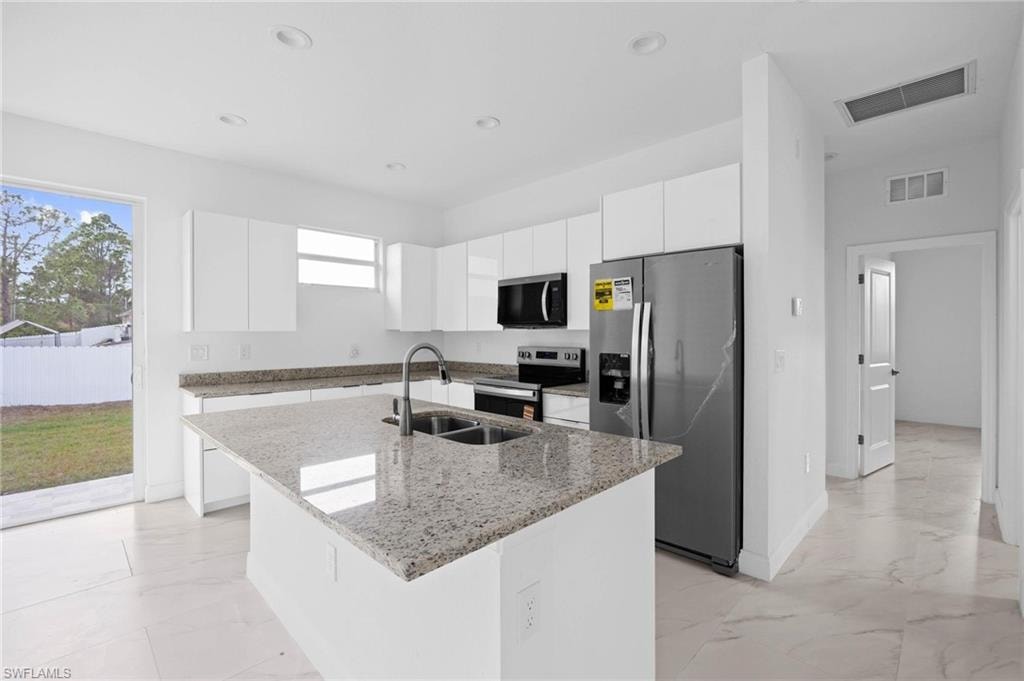 Kitchen featuring white cabinetry, stainless steel appliances, light stone counters, modern cabinets, and a kitchen island with sink