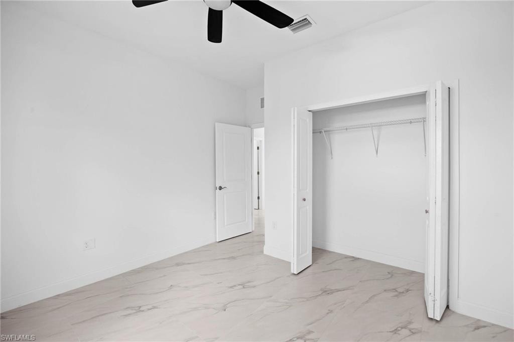 Unfurnished bedroom featuring light marble finish flooring, a closet, and ceiling fan