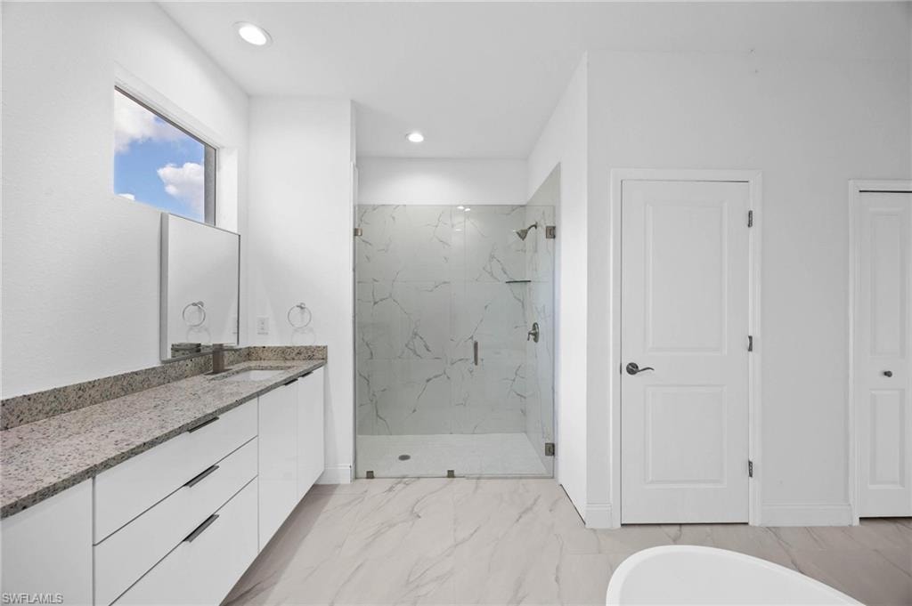 Full bath featuring a marble finish shower, vanity, a freestanding bath, recessed lighting, and light marble finish floors