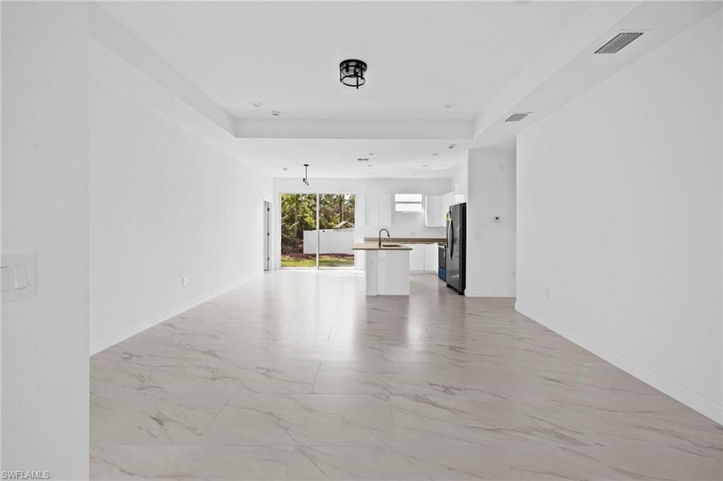Unfurnished living room with a raised ceiling, light marble finish flooring, and recessed lighting