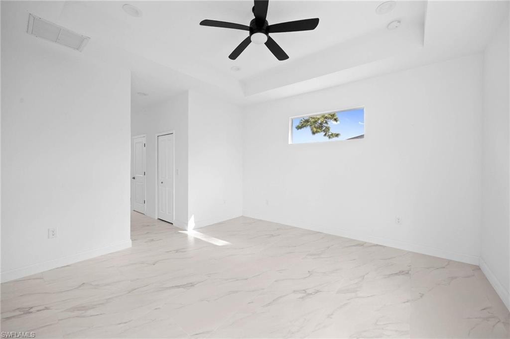 Empty room with light marble finish floors, a raised ceiling, and ceiling fan