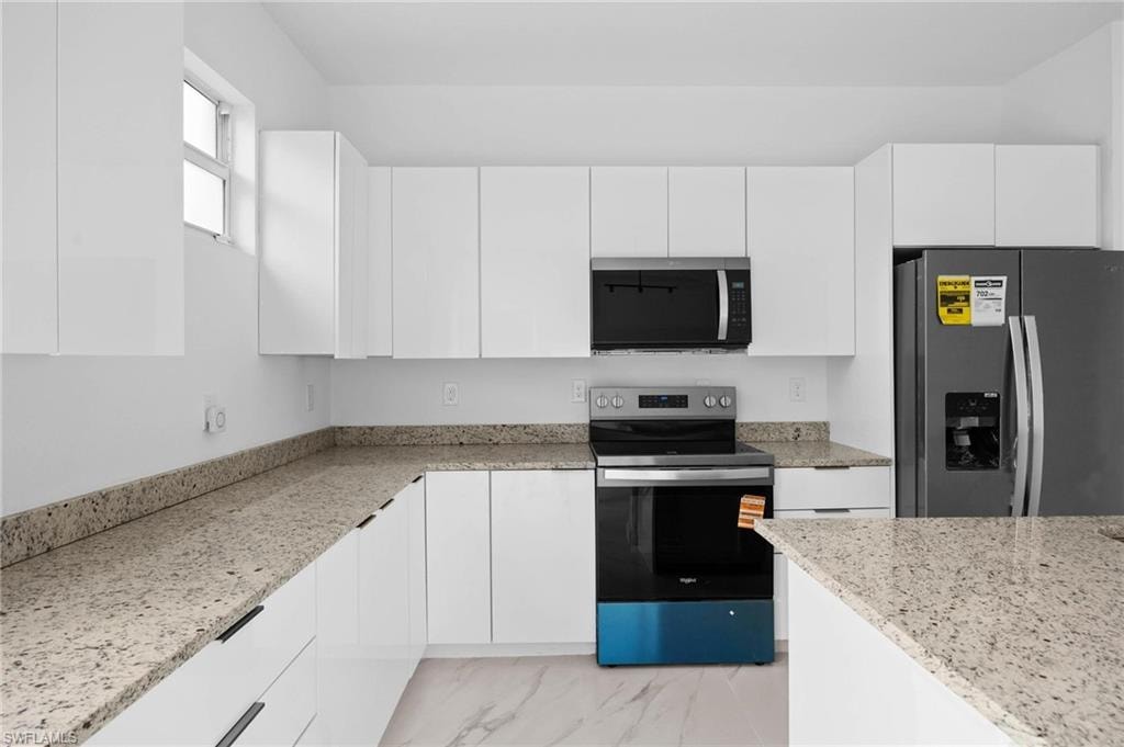 Kitchen featuring stainless steel appliances, modern cabinets, white cabinets, and light stone counters