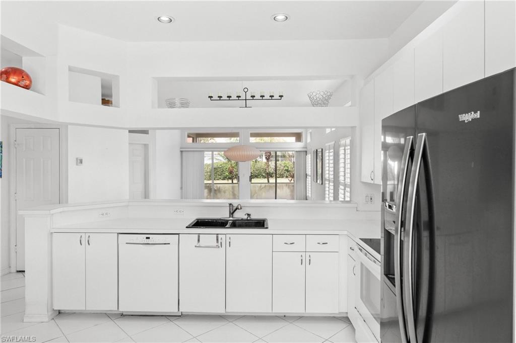 Kitchen with white appliances, white cabinetry, light countertops, a peninsula, and pendant lighting