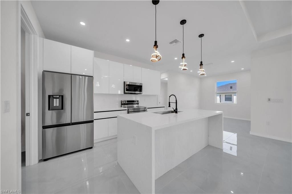 Kitchen featuring stainless steel appliances, white cabinets, pendant lighting, an island with sink, and light stone countertops