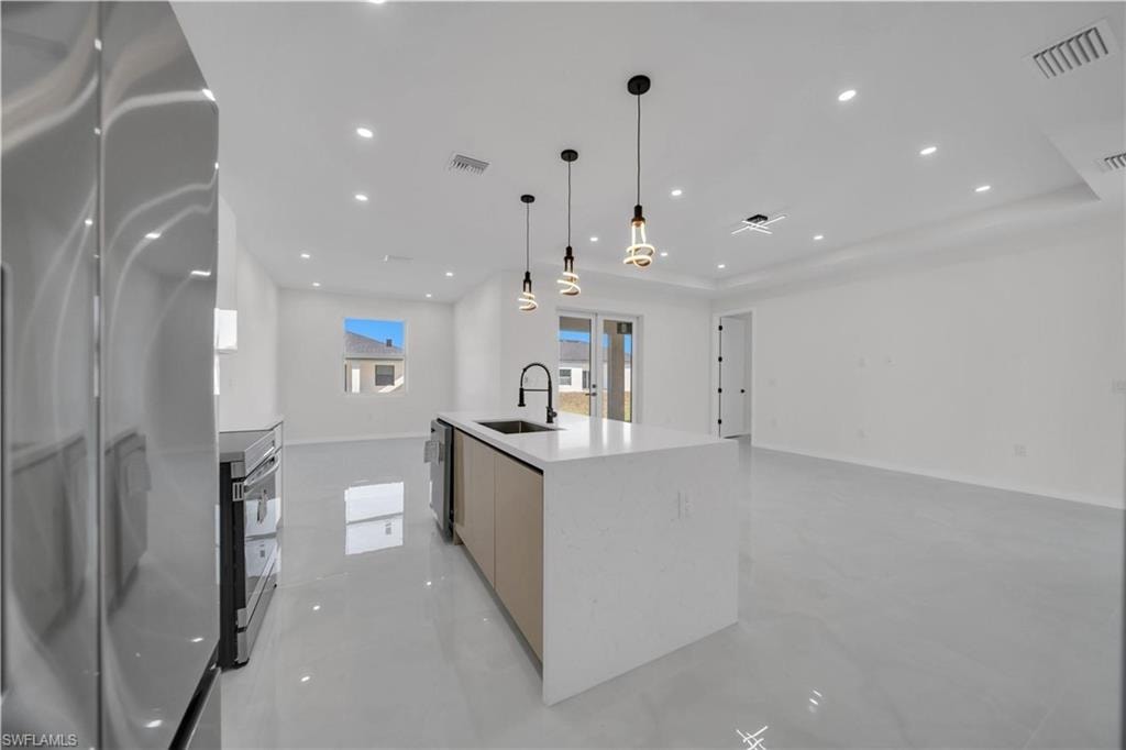 Kitchen with stainless steel appliances, a kitchen island with sink, open floor plan, concrete flooring, and light stone countertops