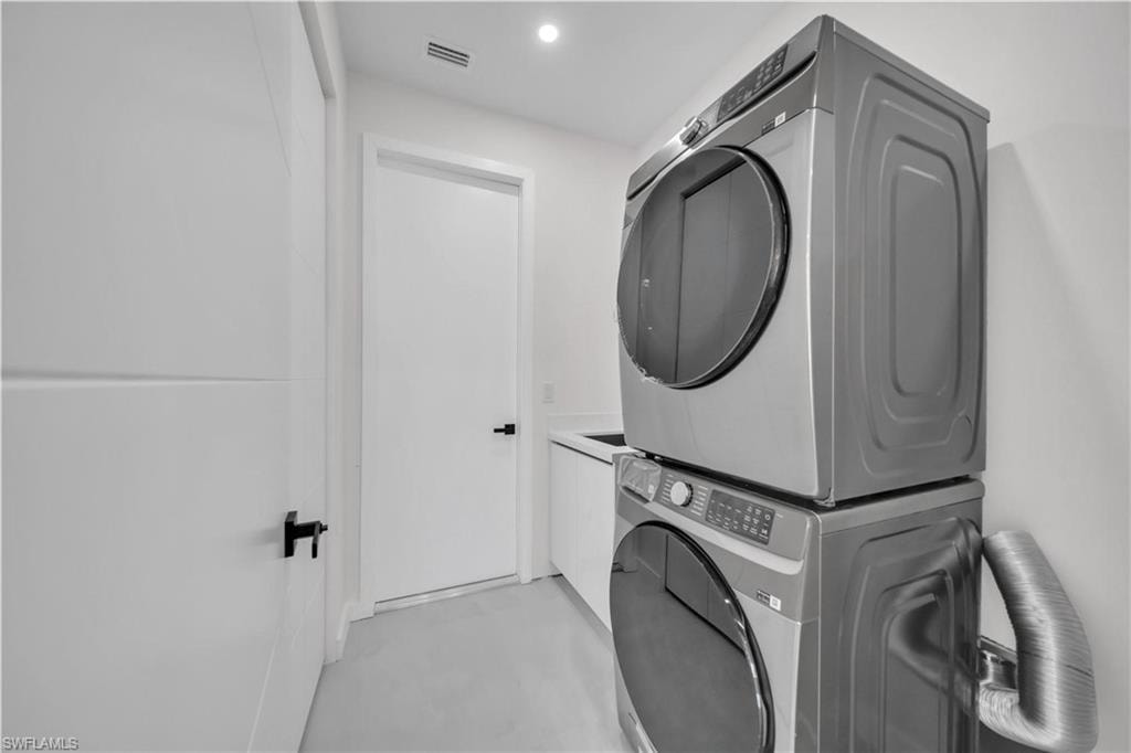 Laundry area featuring stacked washing machine and dryer, finished concrete flooring, cabinet space, and recessed lighting