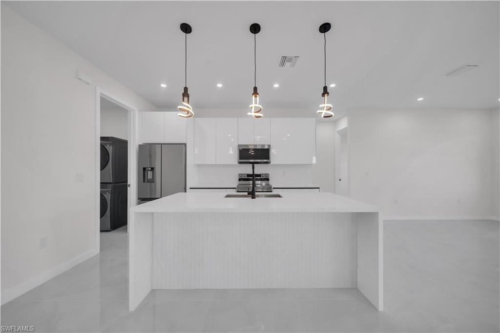 Kitchen with stainless steel appliances, white cabinets, decorative light fixtures, and stacked washer and clothes dryer