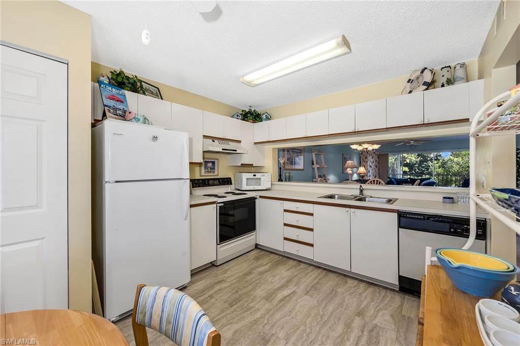 Dual tone kitchen featuring light countertops, white appliances, a textured ceiling, light wood-style floors, and dual tone cabinets