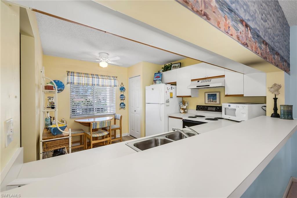 Kitchen featuring light countertops, range with electric cooktop, white cabinetry, freestanding refrigerator, and ceiling fan