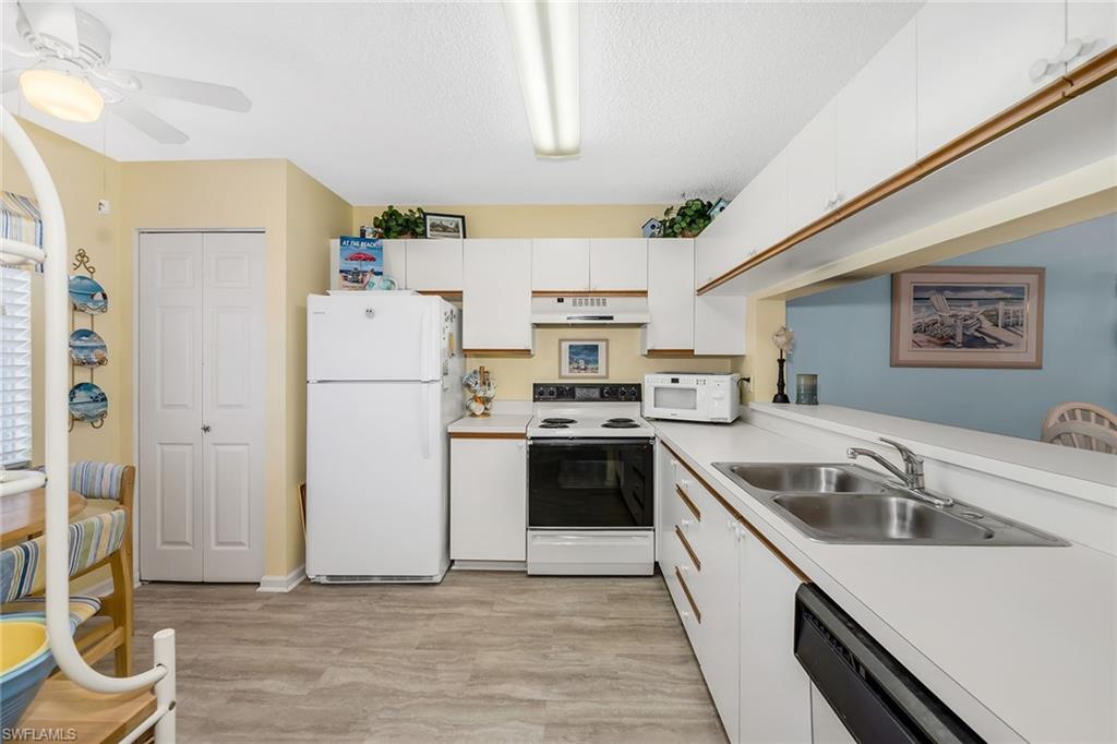 Kitchen with white cabinets, white appliances, light countertops, light wood-style flooring, and a textured ceiling